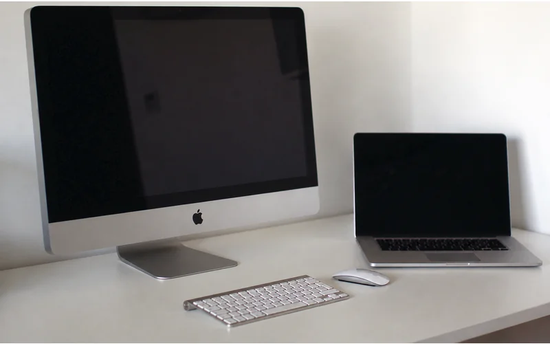 iMac et MacBook ouverts côte à côte, avec clavier et souris sur un bureau blanc